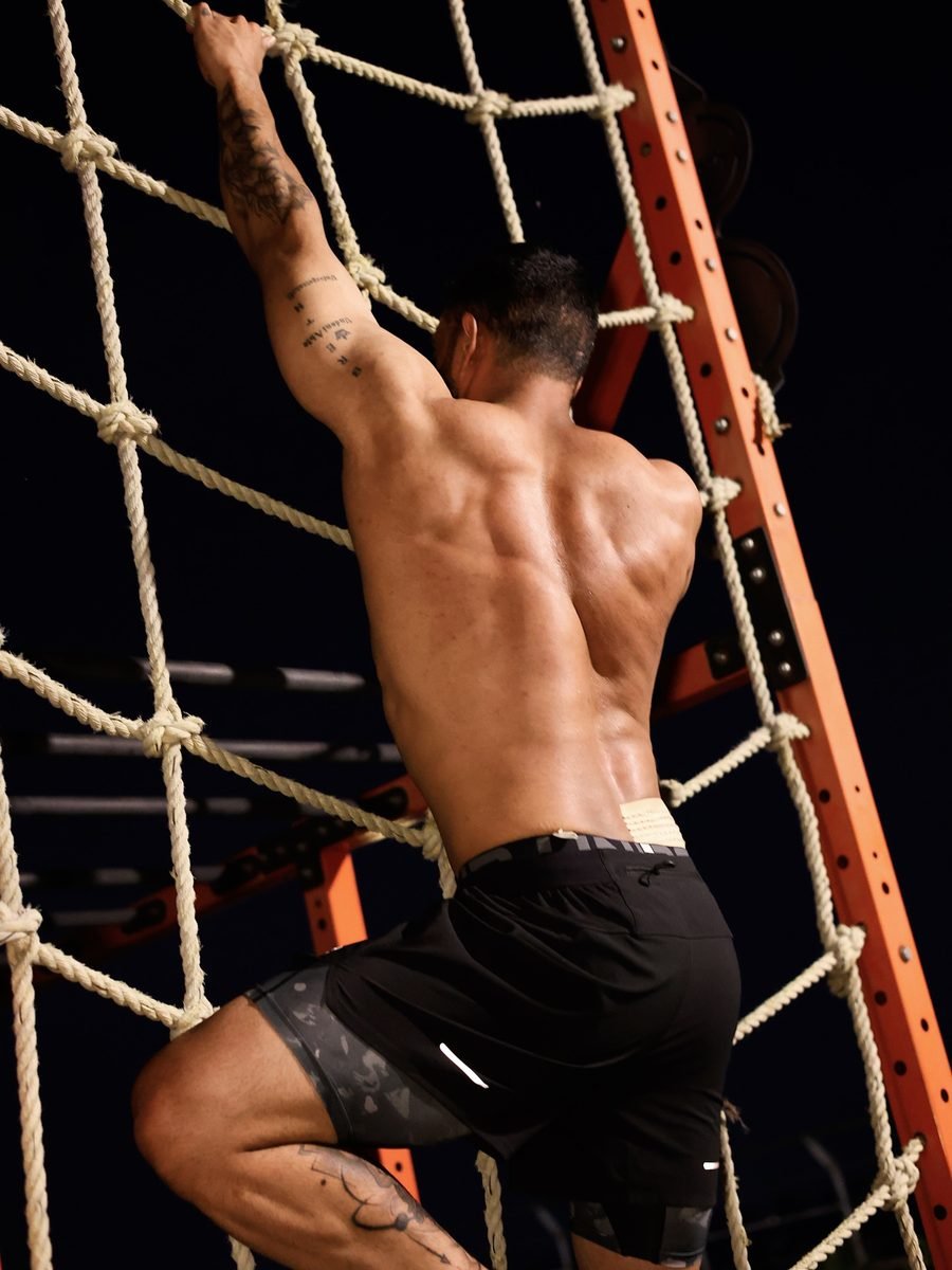 Satnaam pulling himself up a cargo net against a black background