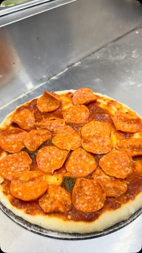 A hand-stretched pizza base topped with sauce and pepperoni on the pass